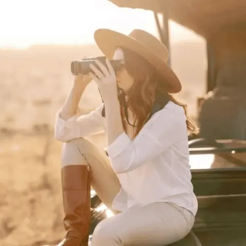 A woman observes wildlife in the savanna through binoculars while on a safari.