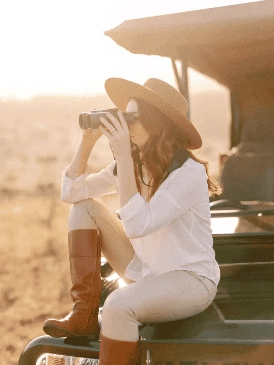 A woman observes wildlife in the savanna through binoculars while on a safari.