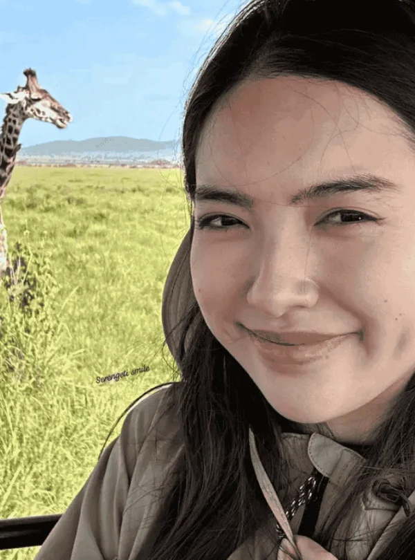 A young woman enjoys a wildlife safari in Lake Manyara National Park with the Maus Safari Company. A giraffe can be seen in the background.