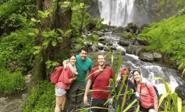 A group of smiling men and women pose in front of an impressive waterfall. Materuni Waterfalls.