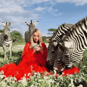 A woman in a red dress stands surrounded by zebras in a natural setting. Serval wildlife day trip